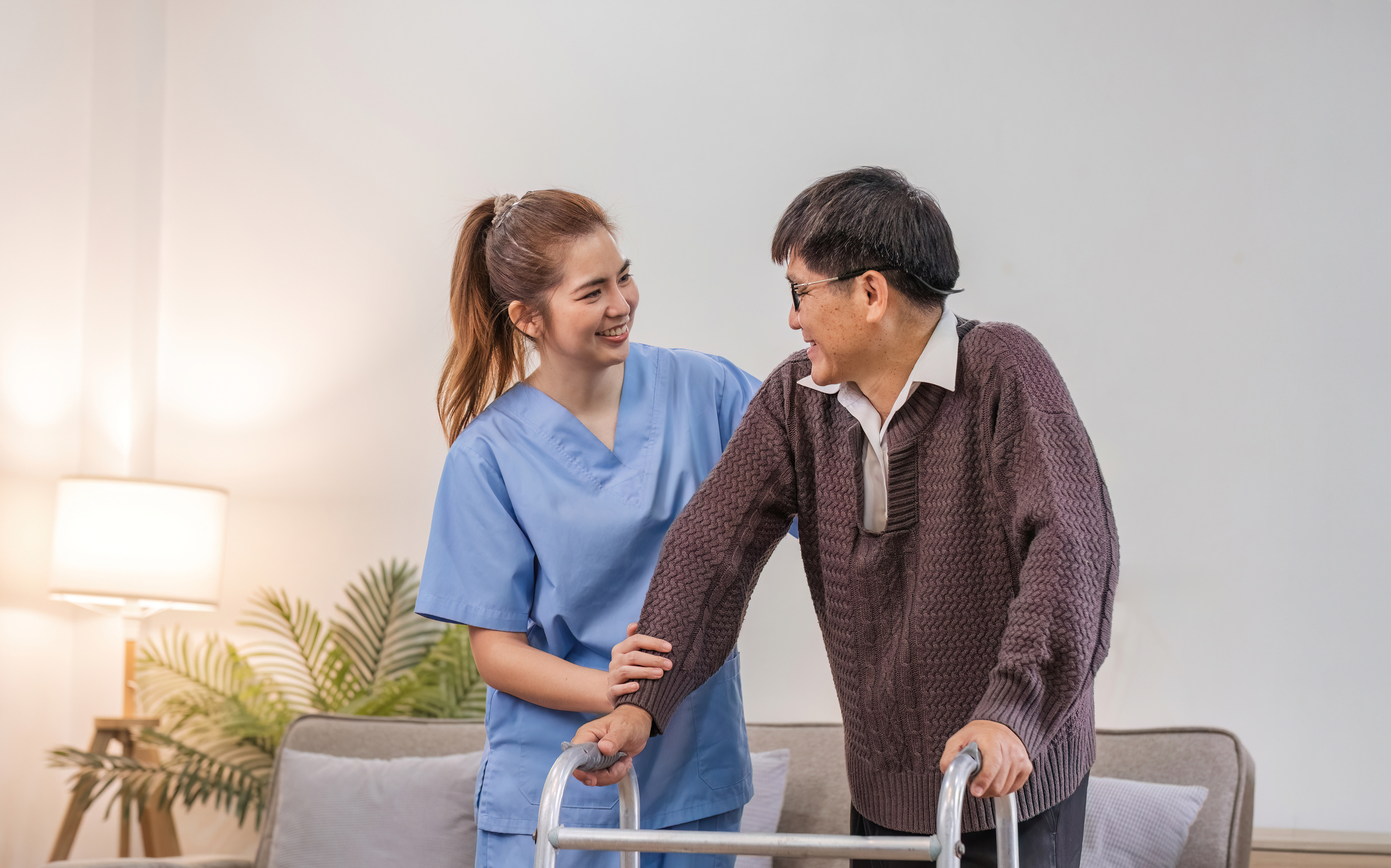 young asian female nurse care giver helping asian senior old man with mobility walker in living area of nursing home senior daycare center. Nurse take care elderly patient with cheerful concentrate